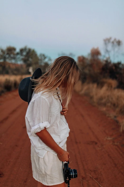 girl holding camera on dirt road at dusk