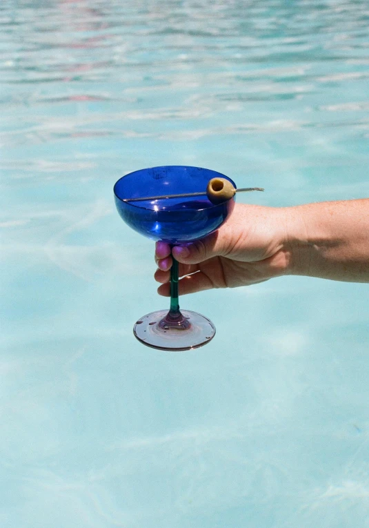 a person holding a wine glass with an olive on it