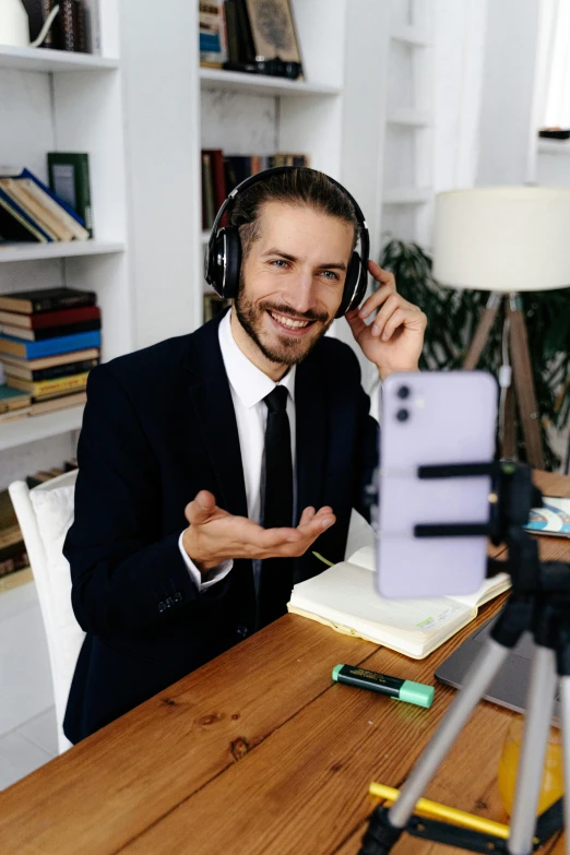 a man in a suit sits at a desk wearing headphones