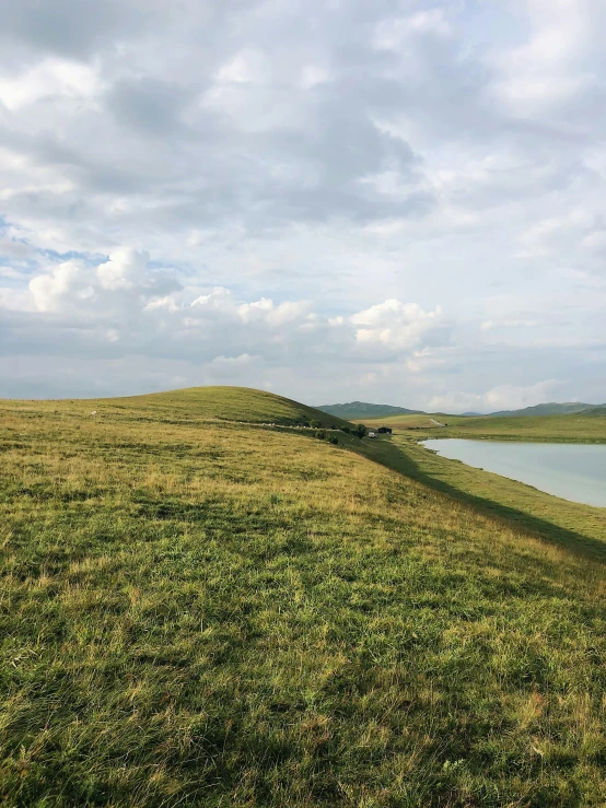 grassy hill, lake, and cloudy sky near water