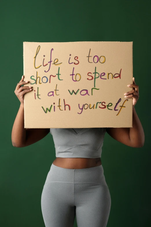 an adorable woman wearing grey sports wear holding up a sign