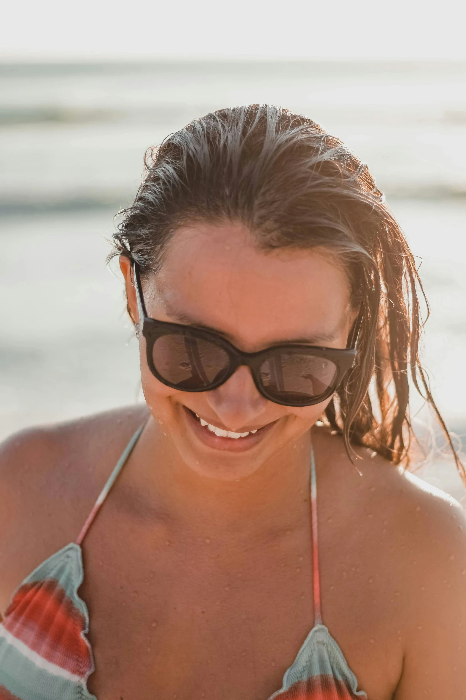 a woman smiling in the sand while wearing sunglasses