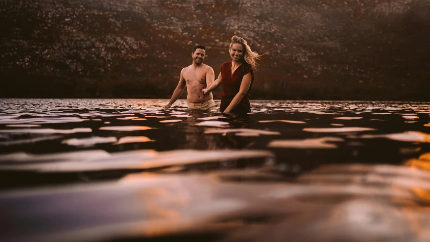 two people wading in the water at sunset