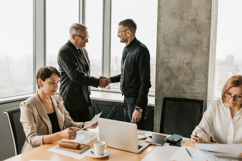 three business people sitting at a table, shaking hands with each other