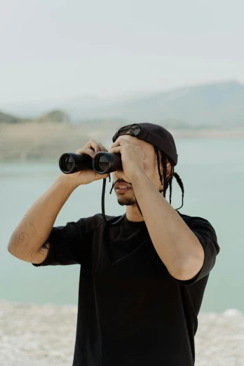 a man is standing by the water looking into binoculars