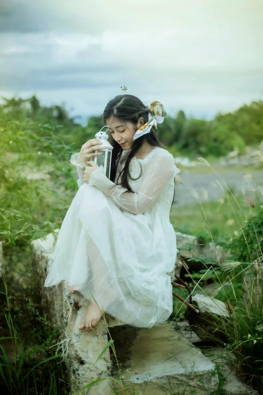 woman in a white dress sitting on a rock and holding a camera