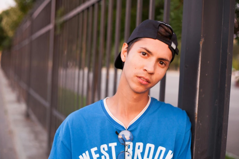 a man in blue shirt and cap standing by fence