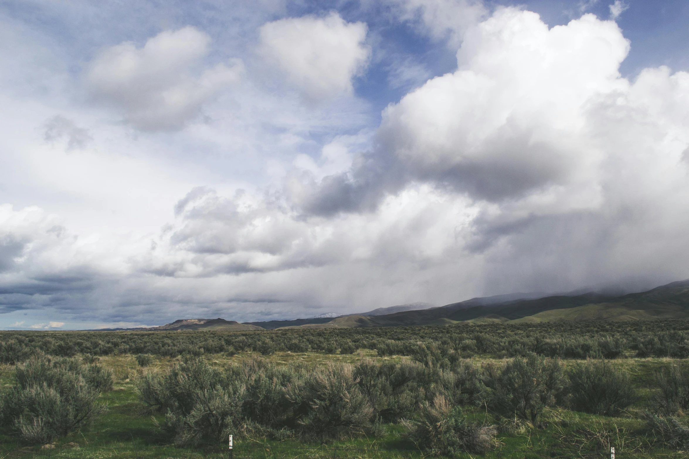 several clouds over hills and a grassy field