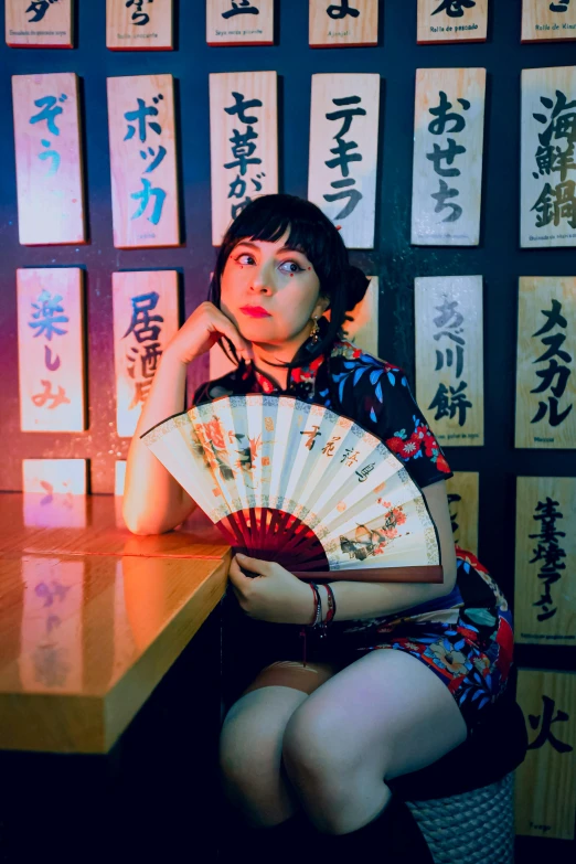 woman in asian attire sitting on table and holding an asian style hand fan