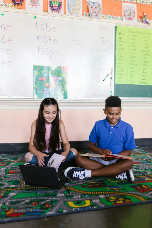 two children sit on a rug in front of a chalkboard