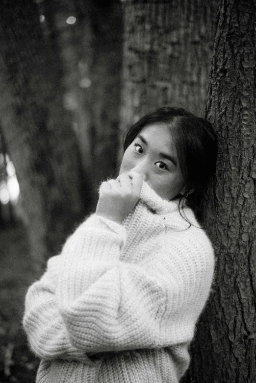 a black and white po of a girl leaning against a tree