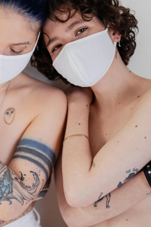 two tattooed women posing for the camera wearing masks