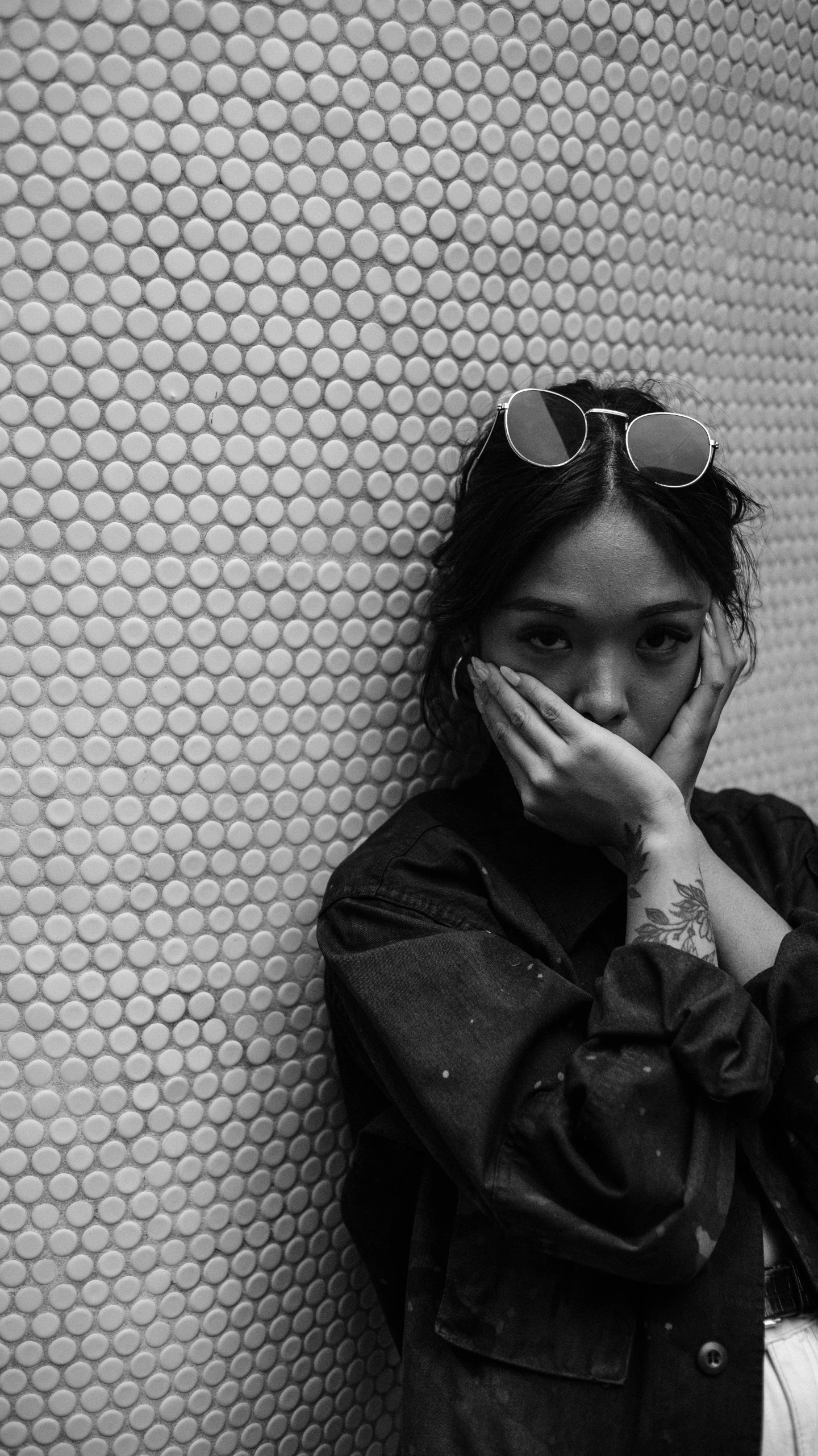 a young woman standing against a wall wearing sunglasses and covering her eyes with her hands