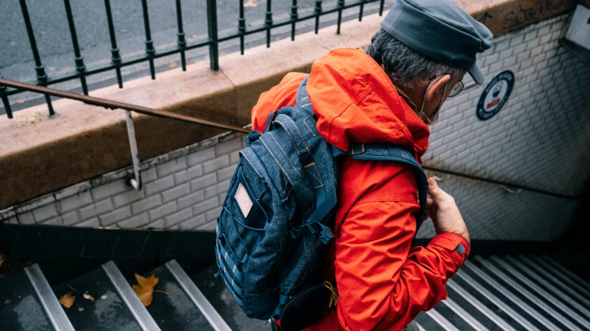 an old man wearing a backpack climbing up a flight of stairs