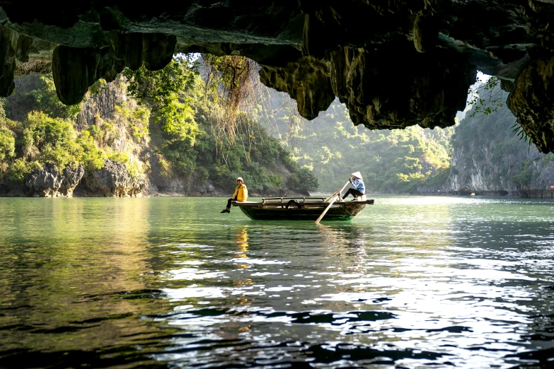 two people riding on the front of a canoe in a bay with some moss growing over rocks