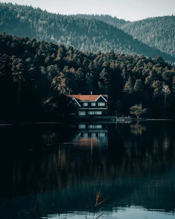 a house on the edge of a lake with mountains in the background