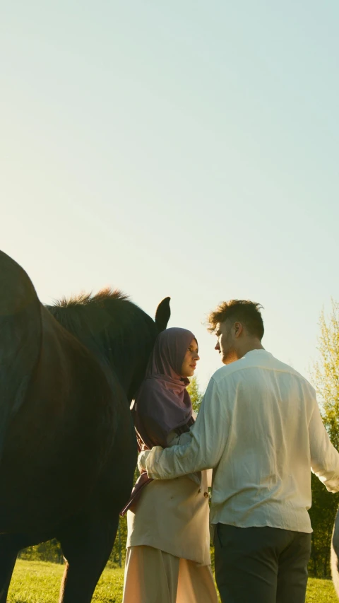 the man and woman are standing close to a horse