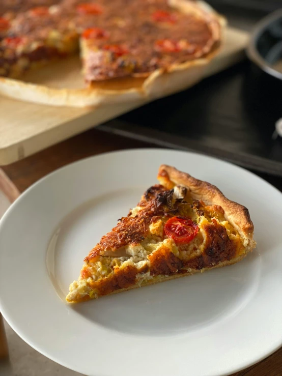 a piece of quiche with tomatoes sits on a white plate