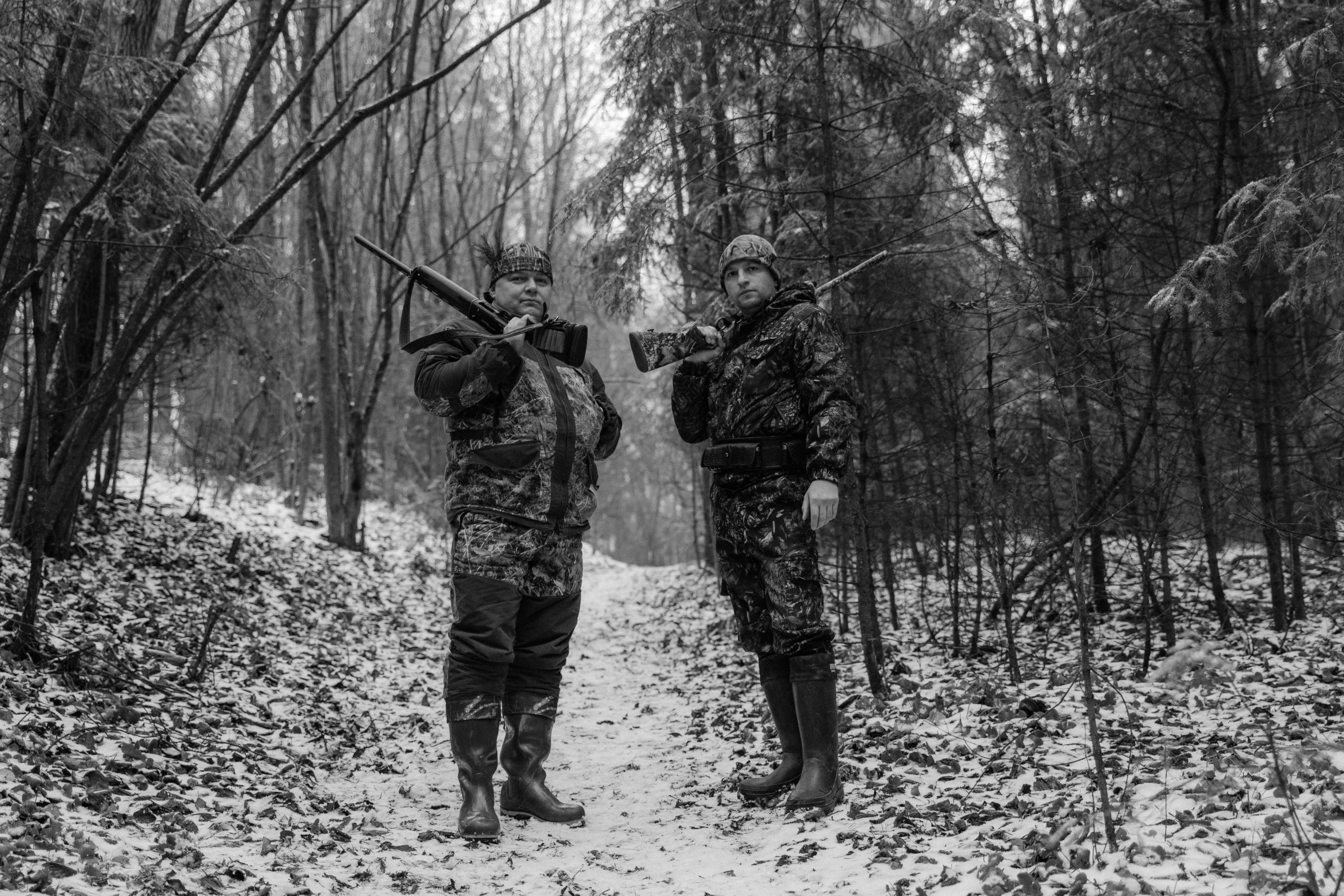 two hunters with guns stand in a snowy forest