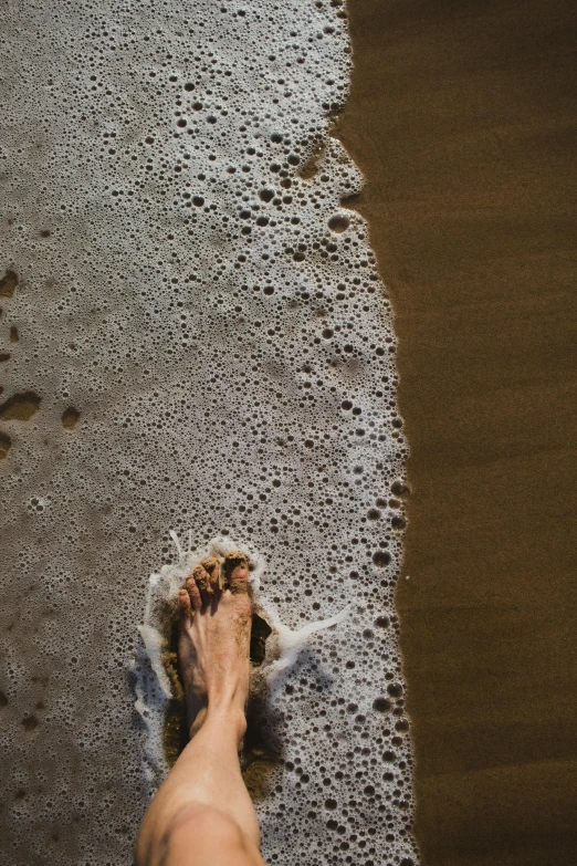 someones bare feet laying on the sand and water