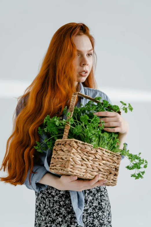 red - haired woman holding basket full of fresh green foliage