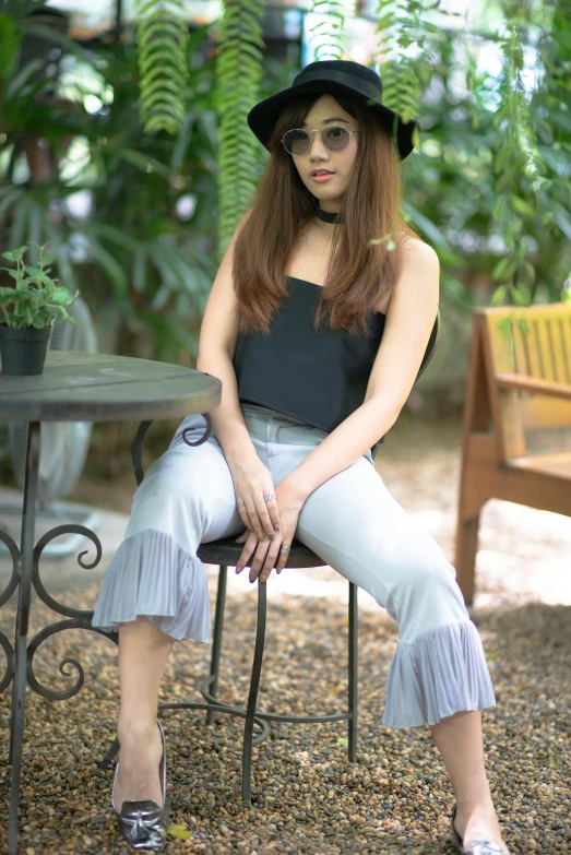 a woman wearing a hat, black shirt and light blue pants sitting at a table