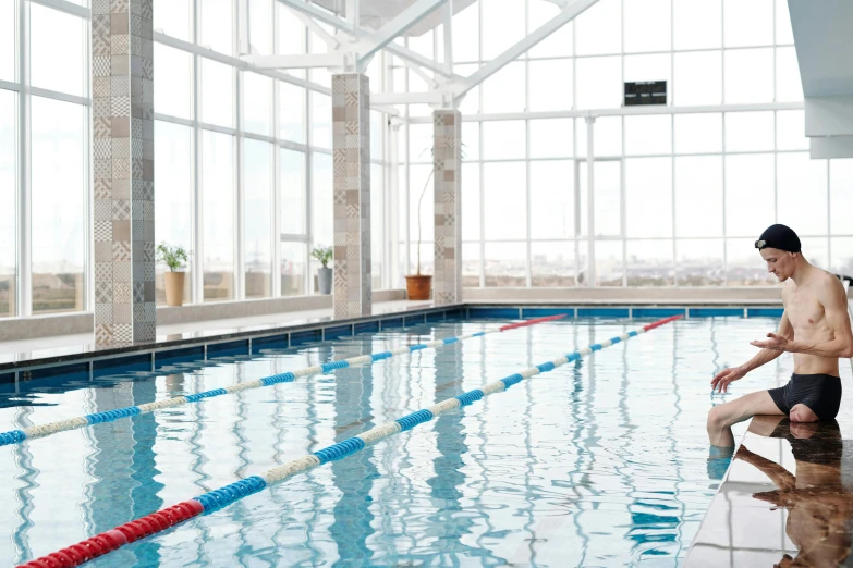 a man in swim trunks sitting by a pool