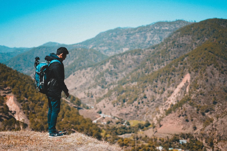 a man in black jacket and backpack on top of a mountain looking at hills