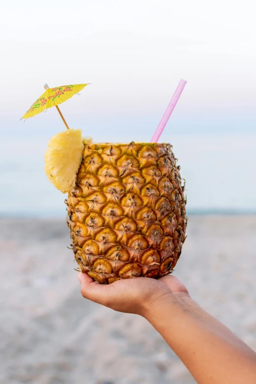 a hand holds up a pineapple with an umbrella