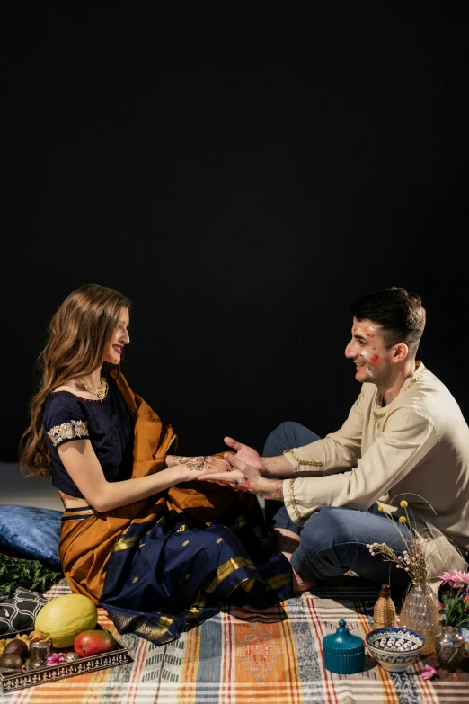 man and woman sitting on a colorful blanket holding hands