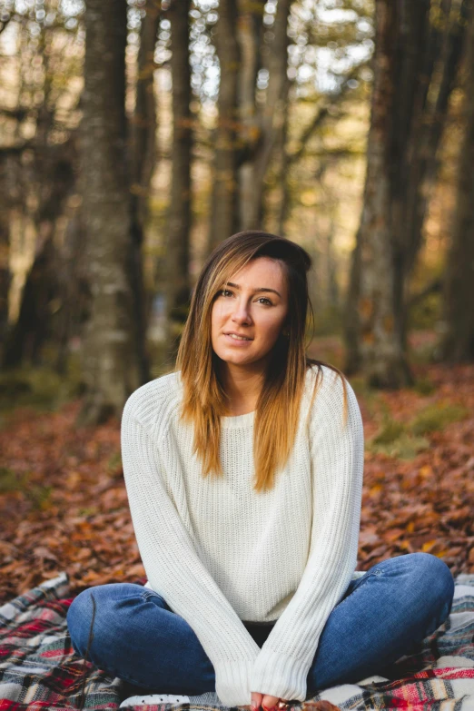 a woman sitting in the woods on a blanket