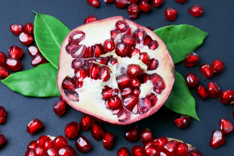 a pomegranate cut open and placed next to the leaves