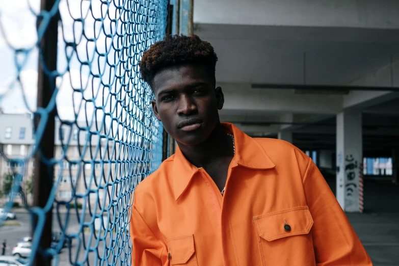 an african american male poses in front of a wire fence