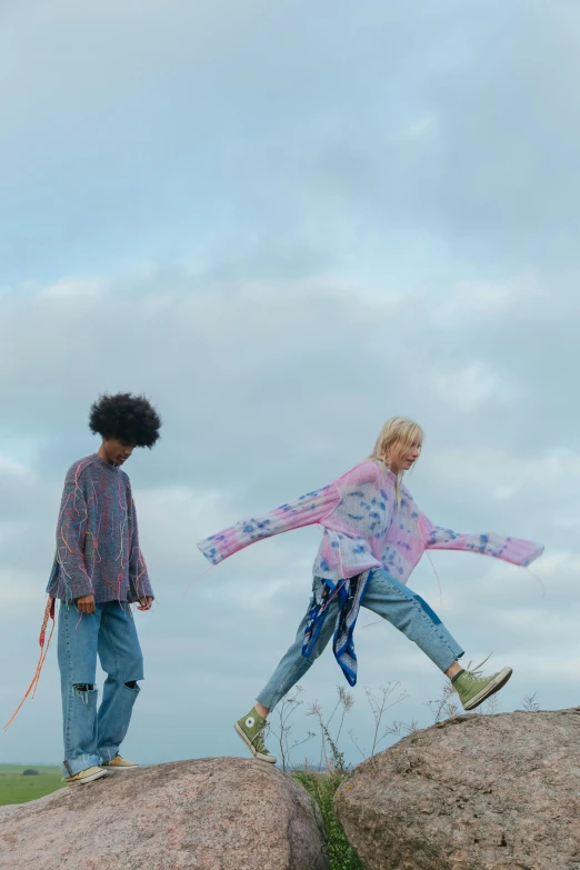 a girl with an afro holding a string and a little girl with a blue shirt hold soing while standing on a rock