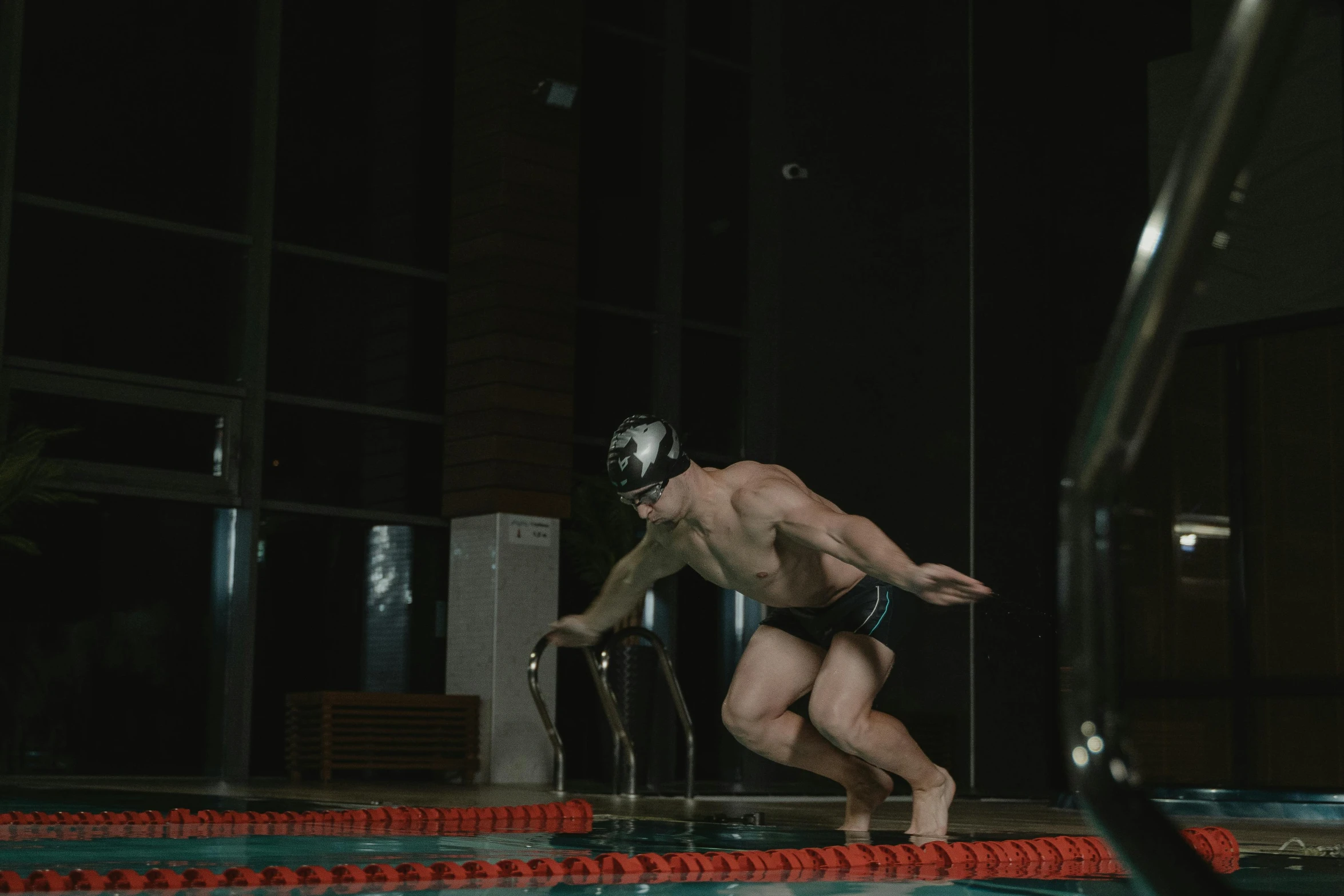 a man with  and swimming goggles stands by the edge of an outdoor swimming pool