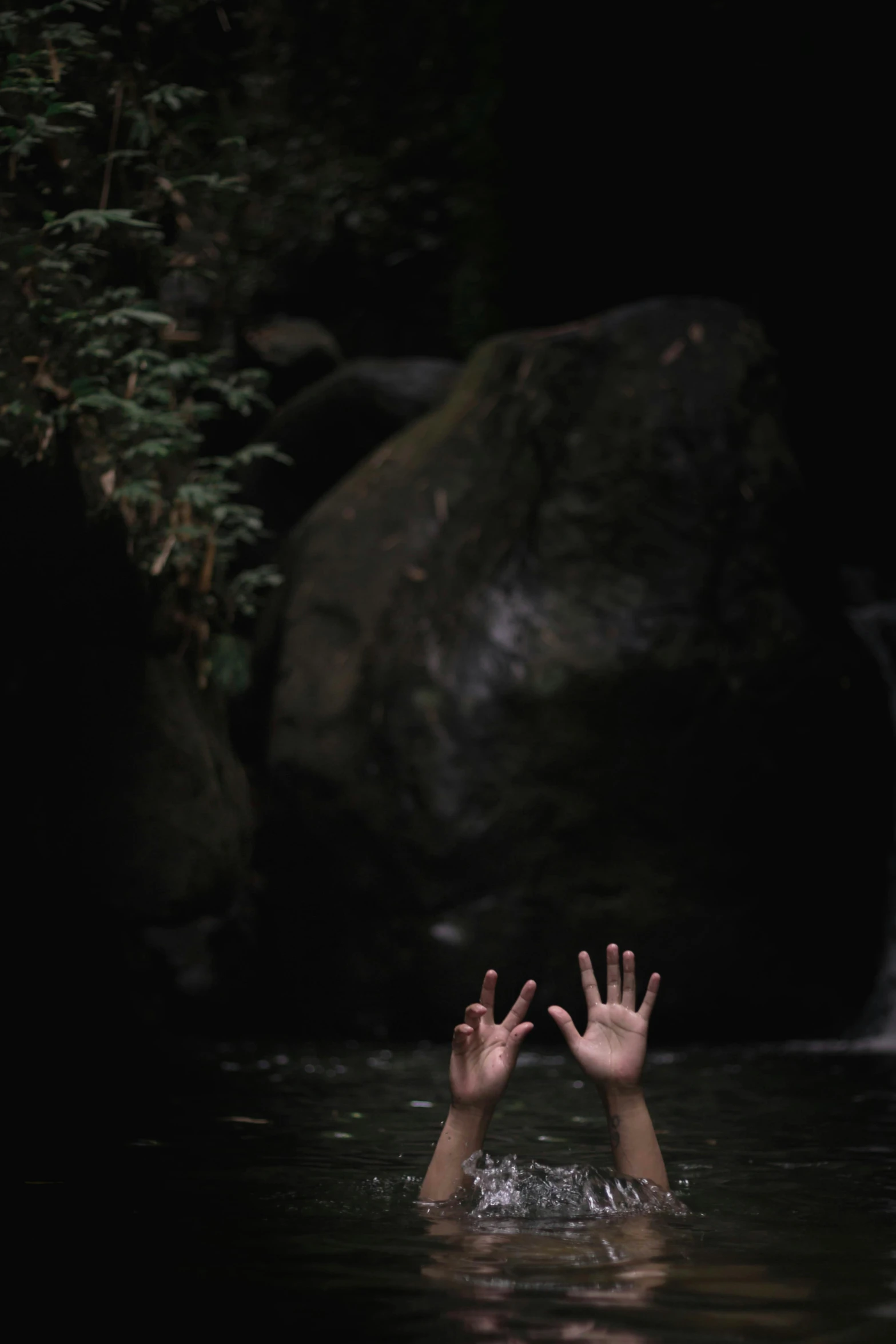 a hand reaching up into the water next to a waterfall