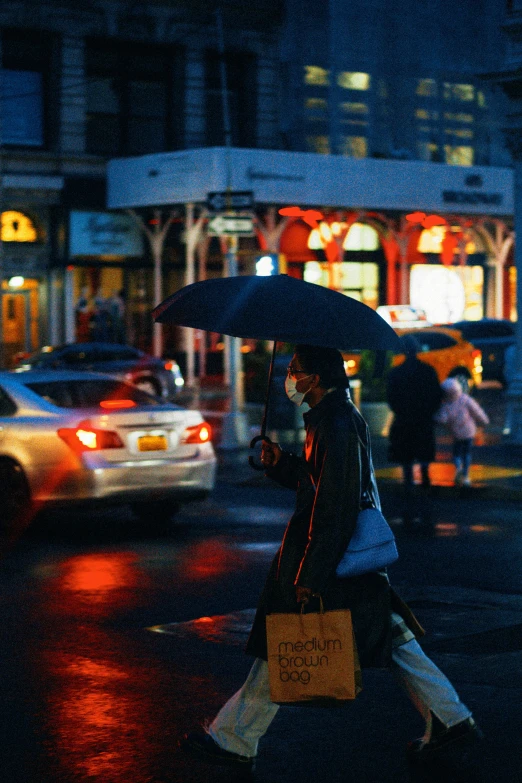 a woman crossing the street in a city at night while carrying an umbrella