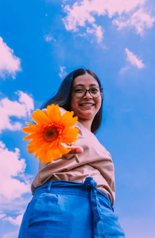 a girl is holding up a large orange flower