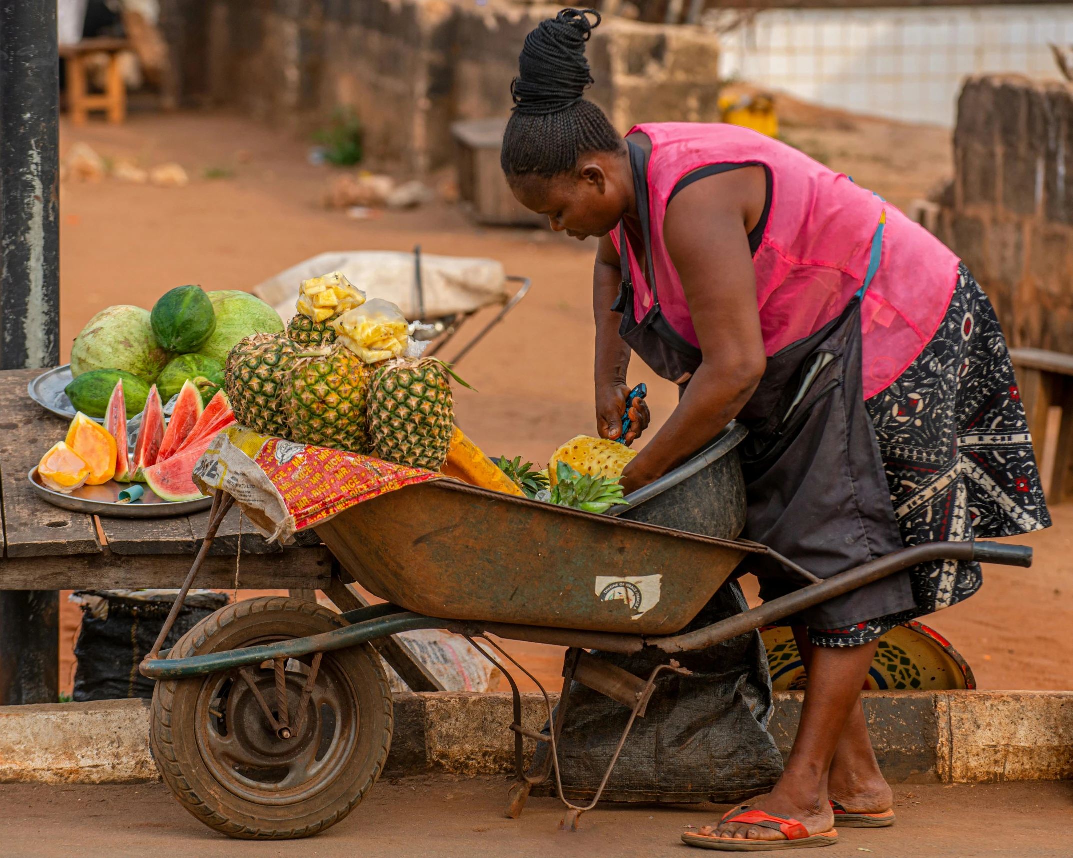 an old black woman is  fruits in her wheel barrow