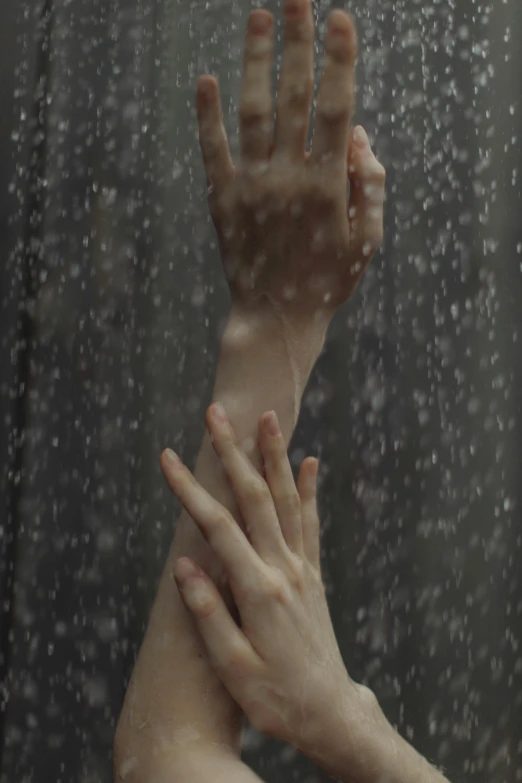 two hands are in the rain behind a glass