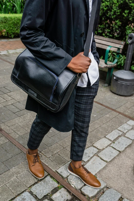 a man in a suit holds his handbag up and walks on a sidewalk