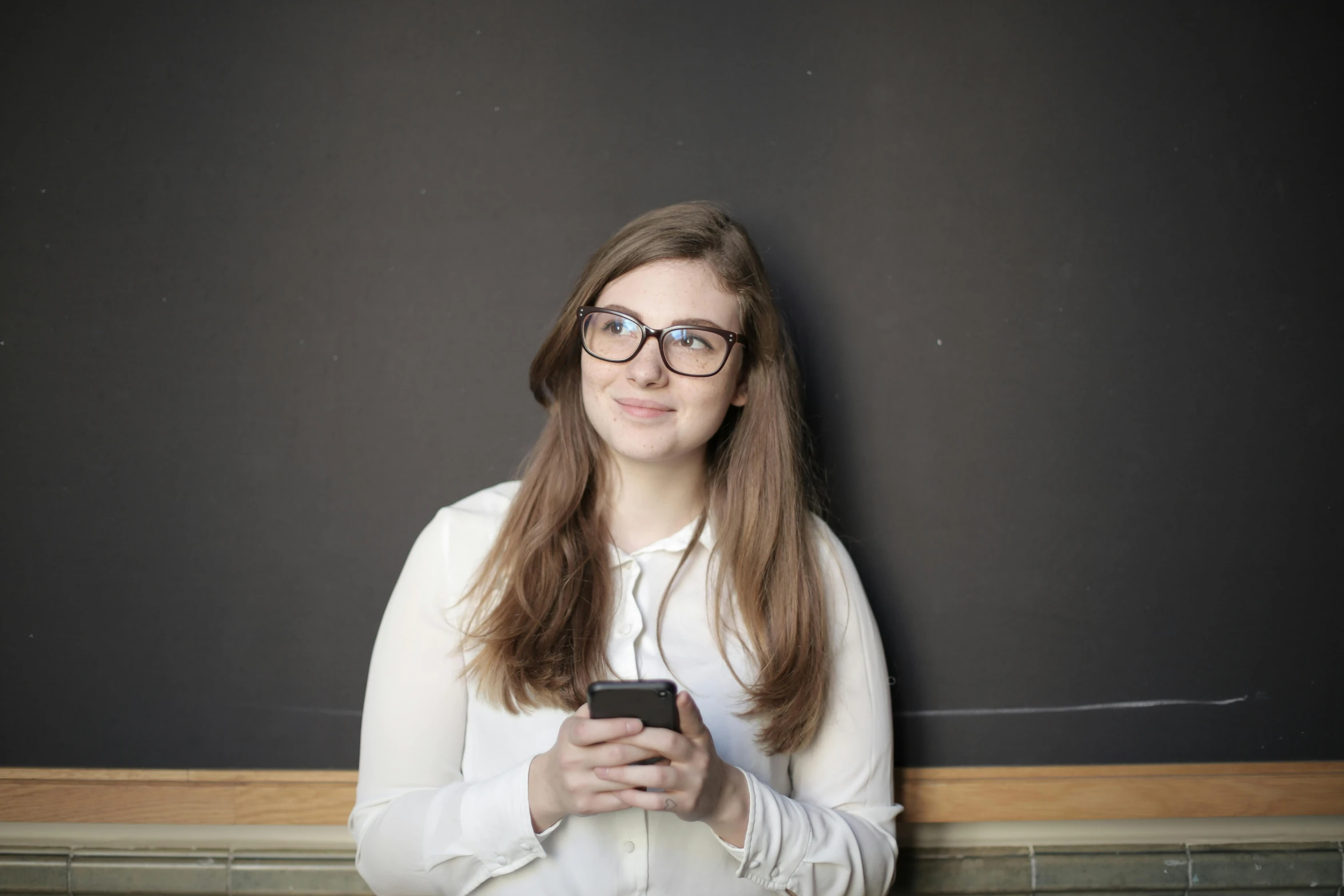 a woman leaning against a wall with a cell phone