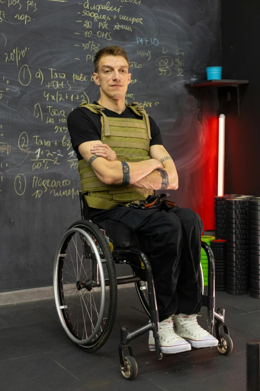 man in wheelchair with hand on hip standing by blackboard