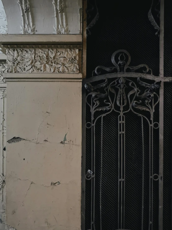 an ornate iron gate near a wall with peeling paint