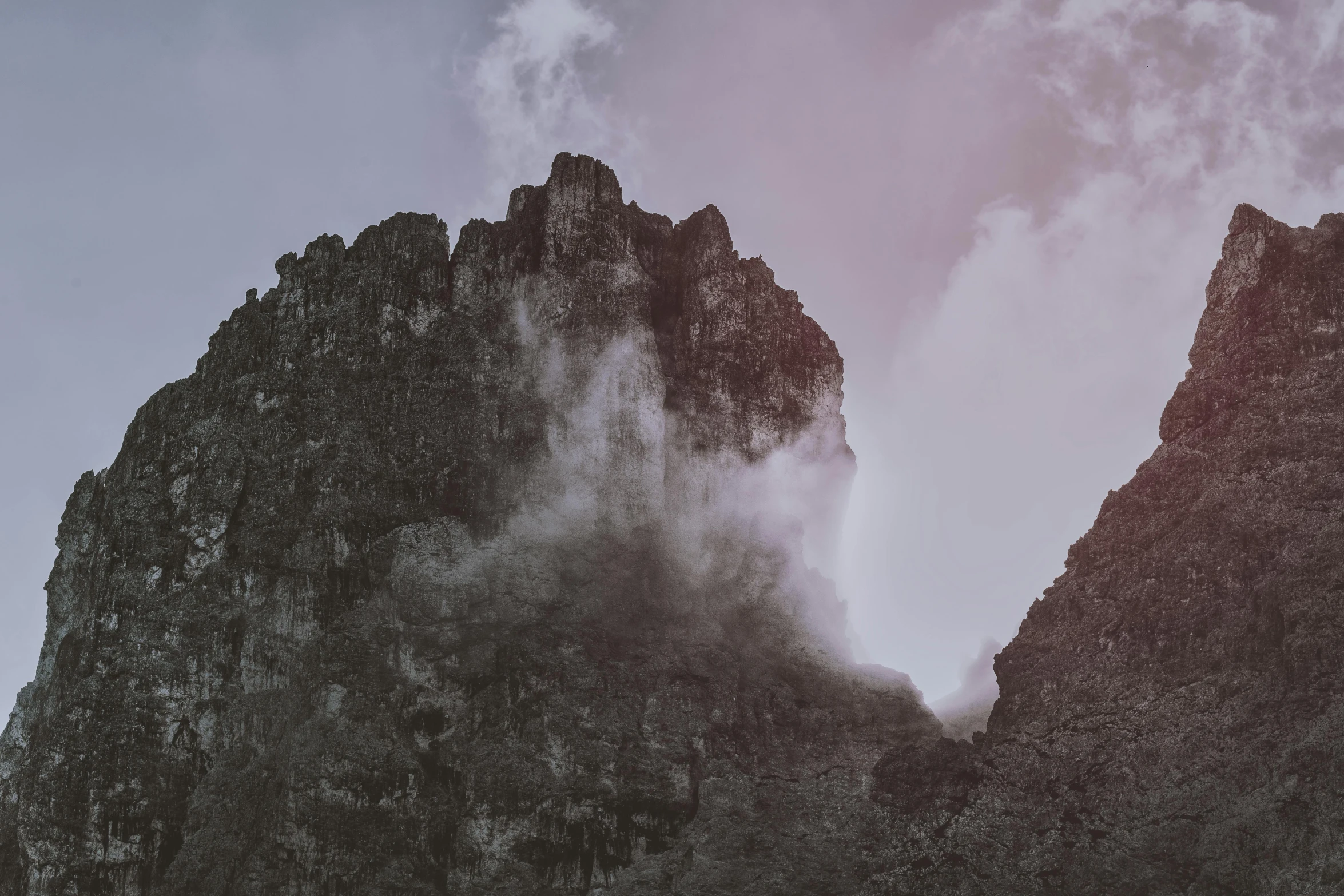 a tall rock formation with clouds coming out of it