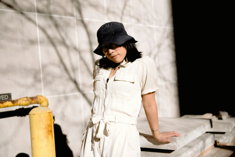 a woman in a hat leans against a fence