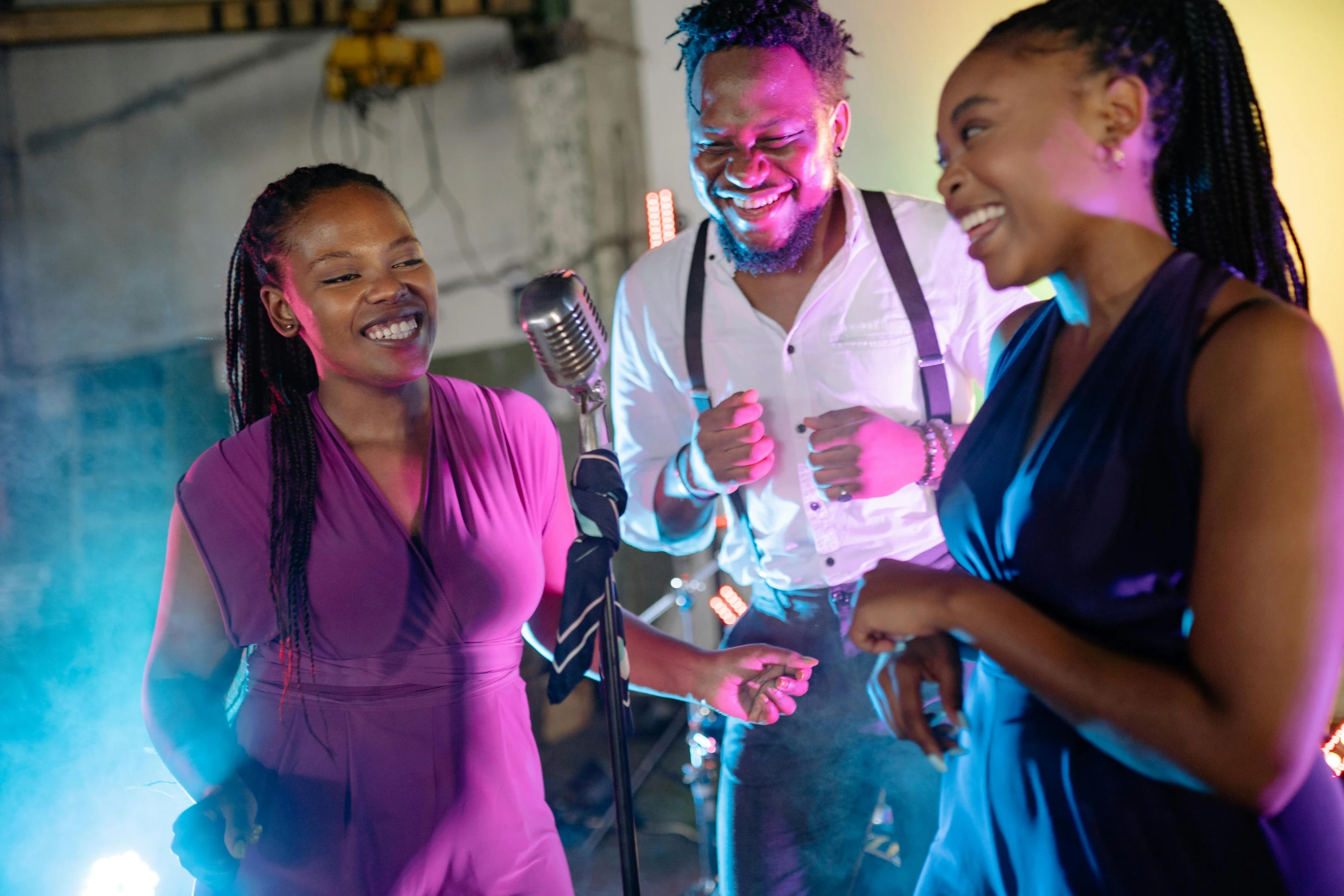 a woman laughs as she and two men sing on stage