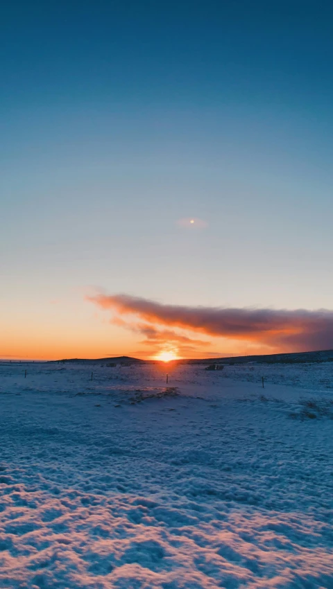 a snow covered hill with the sun setting in the background