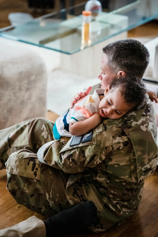 a woman in military fatigues sitting on the ground hugging her son