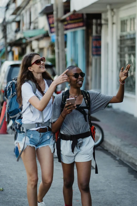 two girls looking at a cell phone together on the street